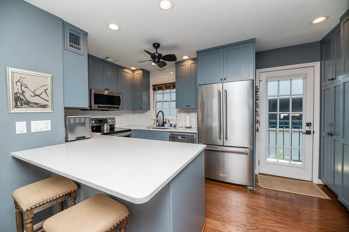 A bright kitchen featuring a central island, stainless steel appliances, and distinctive blue cabinetry. Natural light pours through a window, illuminating the ample workspace, while the arrangement encourages both everyday routines and social gatherings.