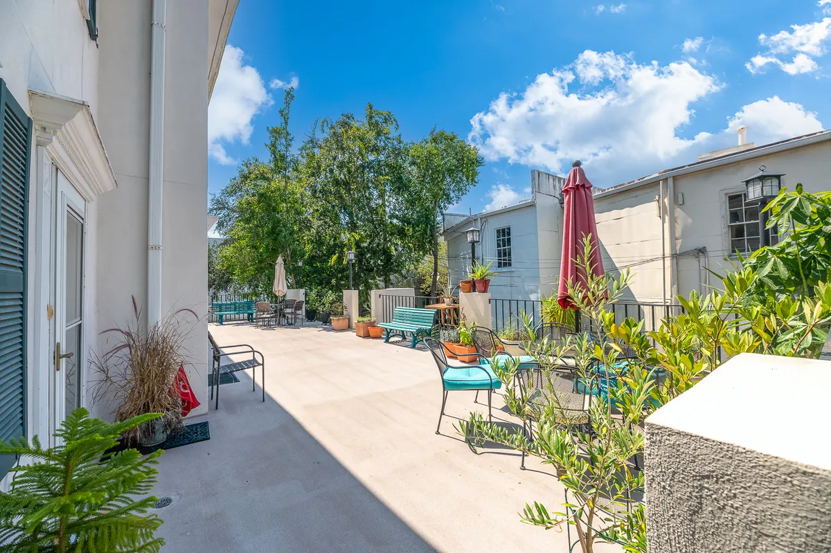 This image provides a clear view of a secluded back patio adorned with comfortable outdoor seating, large trees providing natural shade, umbrellas for added comfort, and decorative planters. The setting exudes tranquility and privacy, making it perfect for relaxation or small social gatherings. Subtle elements hint at the possibility of enjoying meals, reading, or simply soaking in the sunset amidst lush greenery.