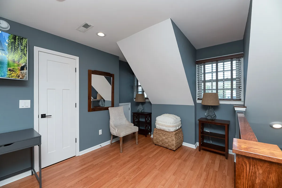 A cozy interior featuring a modern armchair, decorative mirror, flat-screen TV, woven basket, and a window with blinds. The space feels inviting and offers a tranquil nook for reading or relaxing after a day of exploring.