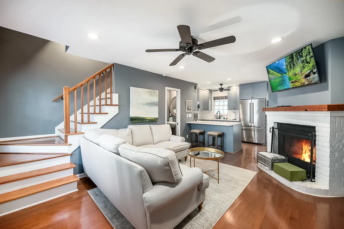 A welcoming open-concept space that seamlessly combines the living room, dining area, and kitchen. The focal points include a comfortable sofa facing a fireplace, a television, and a modern kitchen area. Natural light streams in, enhancing the inviting ambiance and highlighting the open layout and tasteful décor.