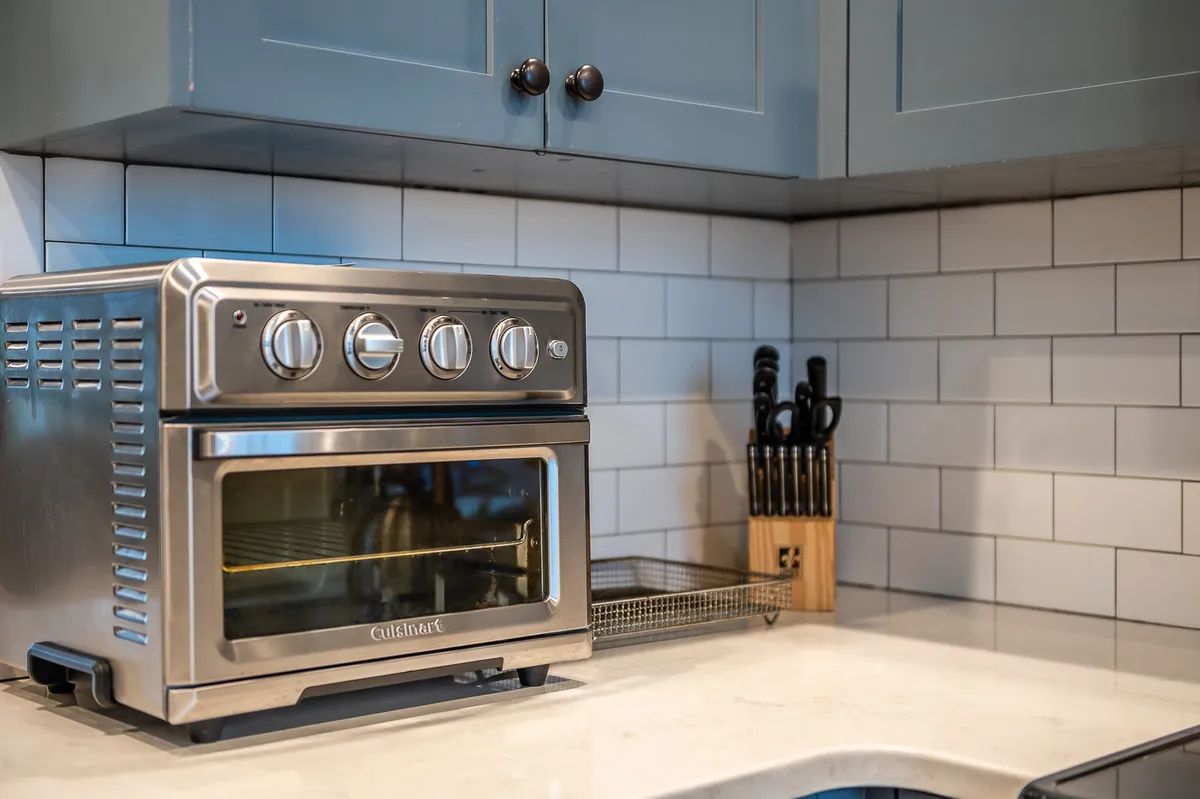 A close-up view of the kitchen's stainless steel oven, blue cabinetry, white subway tile backsplash, and a knife holder, creating a sense of both utility and homeliness. The practical layout and elements make the space ideal for meal prep and creativity.