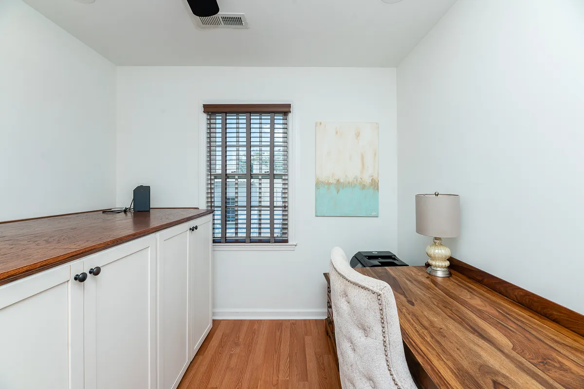 A calm, thoughtfully designed workspace featuring a wooden desk, lamp, window blinds, and wall art. The setup is perfect for catching up on work or enjoying quiet moments between city outings.